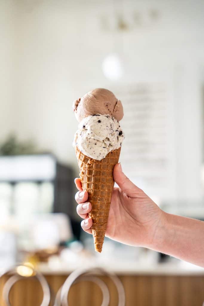 A hand holding up a two-scoop ice cream cone in Savor Ice Cream